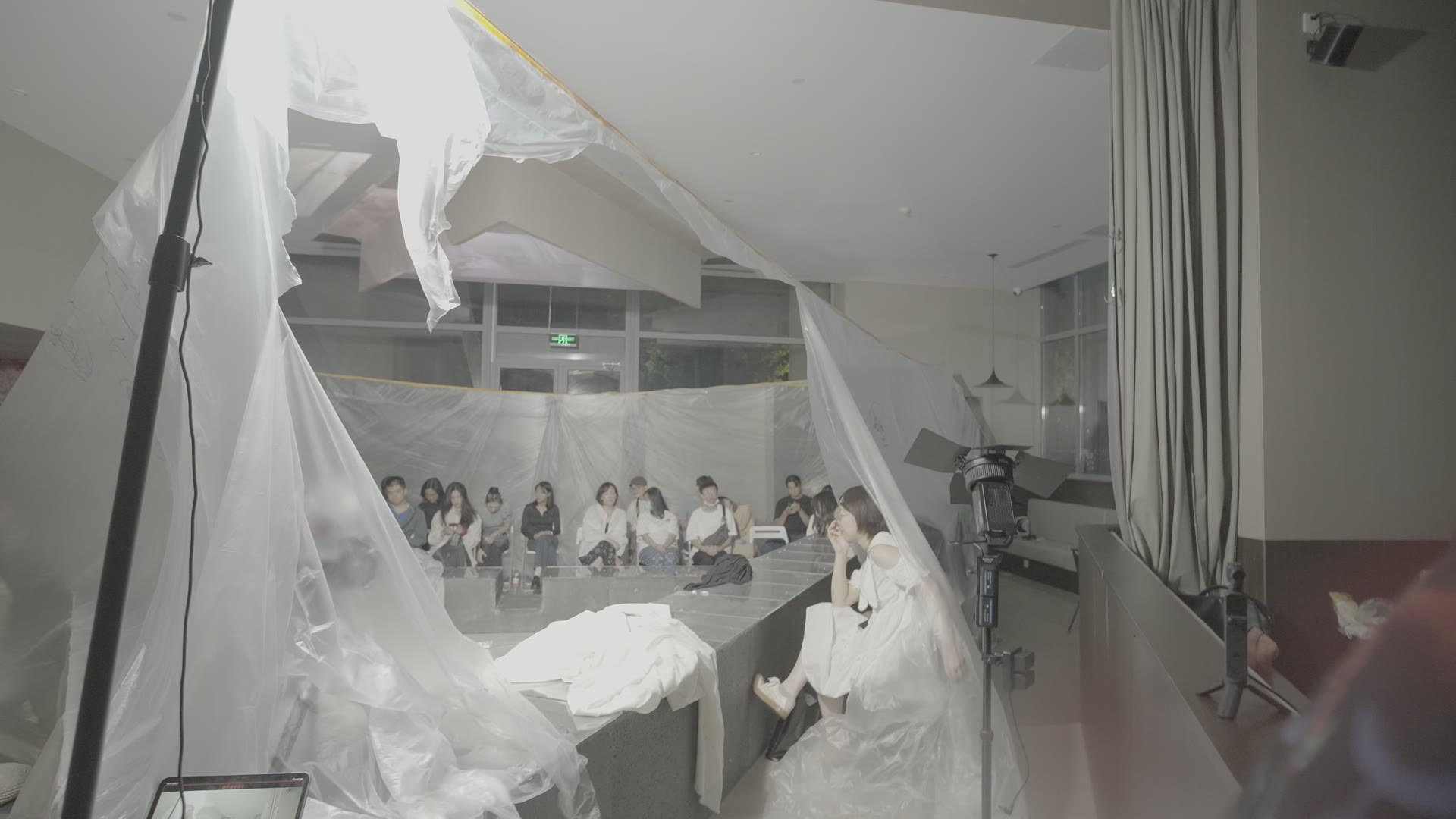 观看者、透明遮隔与照明器材同处一个完整画框。前景是灯具与灯架。